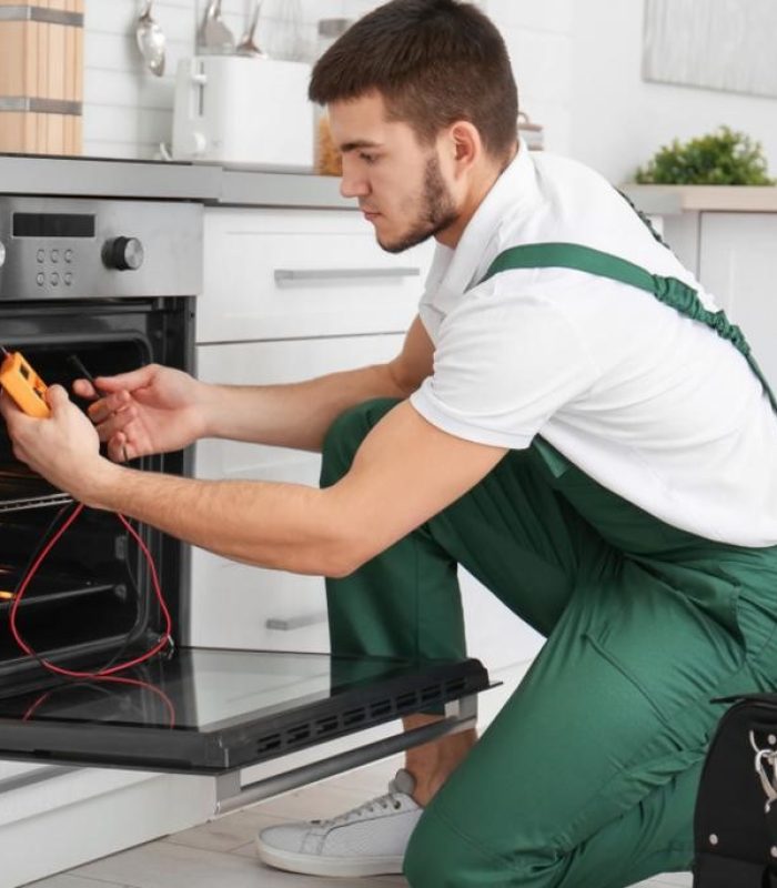 Young man with multimeter repairing oven in kitchen; Shutterstock ID 1012061971